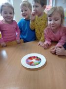 Dzieci obok stolika patrzące jak z cukierków powstaje tęcza.