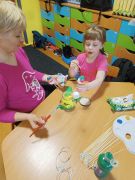 Mama z córką wspólnie malują jajka do stroika. 