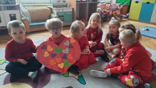 dzieci siedzą na dywanie z papierową laurką w serca