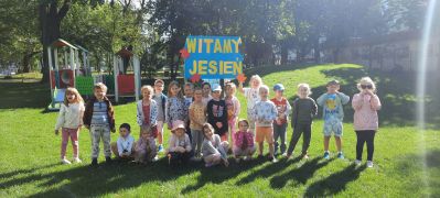 Dzieci pozują na placu zabaw z plakatem Witamy Jesień