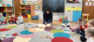 Dzieci siedzą na dywanie i słuchają Pani Ratownik