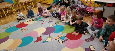 Dzieci siedzą na dywanie i słuchają studentek Stomatologii.