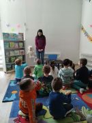 Dzieci siedzą na dywanie i słuchają Pani przewodnik.